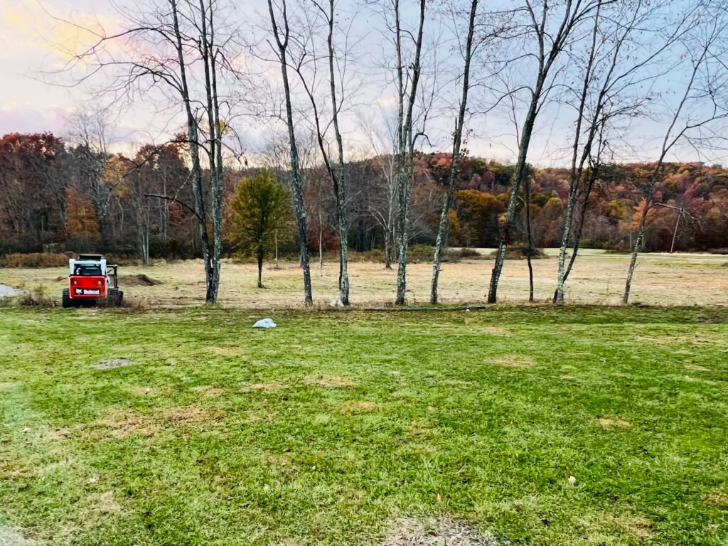 A tractor is clearing trees beside a field, surrounded by greenery and open space.