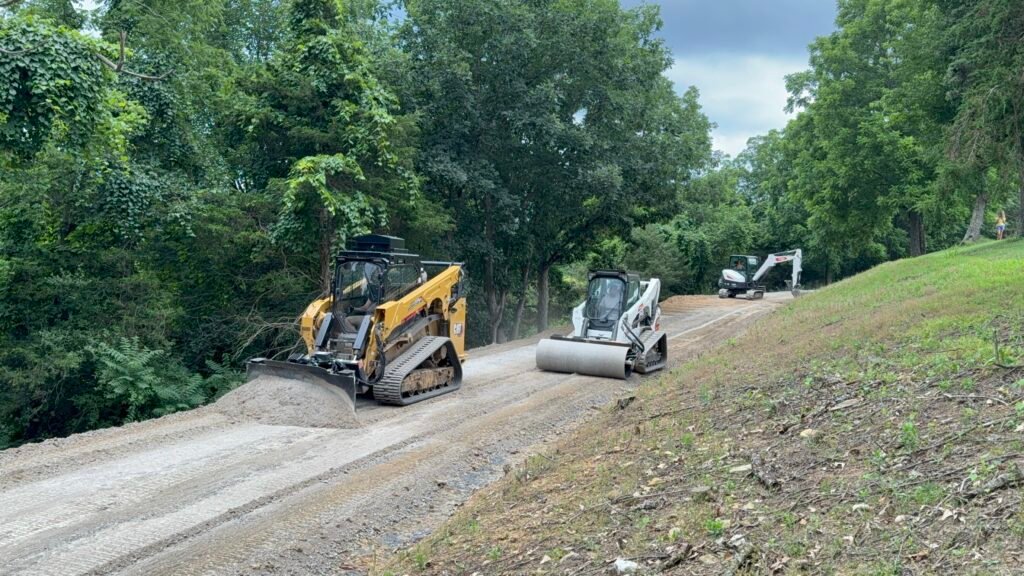 Two construction vehicles are parked on a dirt road, surrounded by a construction site and scattered debris.