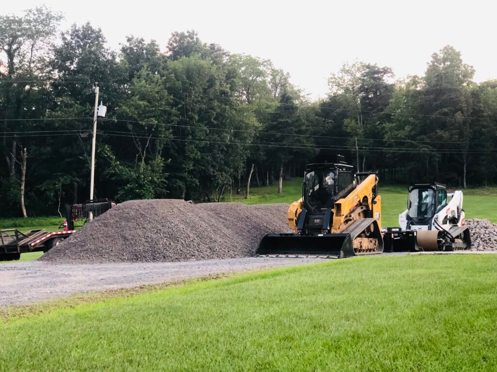 Two construction vehicles on a dirt road, with one excavator and one dump truck visible in a work zone, are maintaining roads and pads.