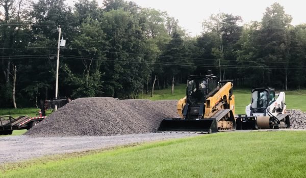 Two construction vehicles on a dirt road, with one excavator and one dump truck visible in a work zone, are maintaining roads and pads.